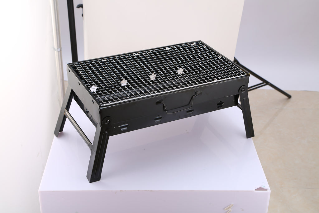 Black charcoal grill with wire cooking grate and foldable legs on tabletop