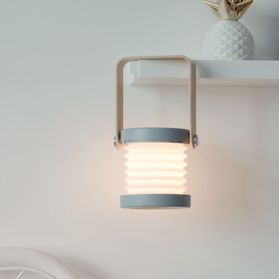 Foldable LED night lantern with warm glow, white ridged body, wood carry handle