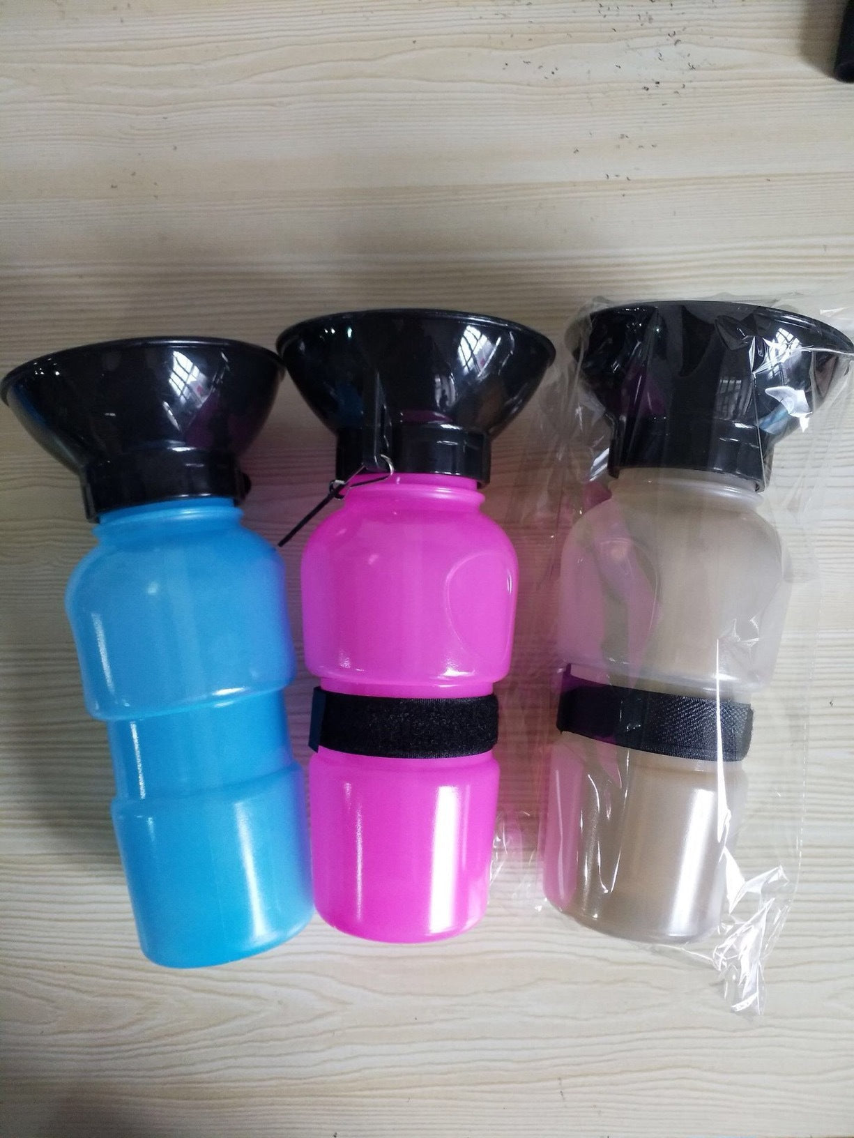 Portable pet water bottle set with black bowls: blue, pink, and clear cups with straps.
