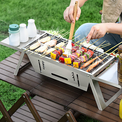 Portable charcoal grill with cooking grate, stainless steel body, and side supports
