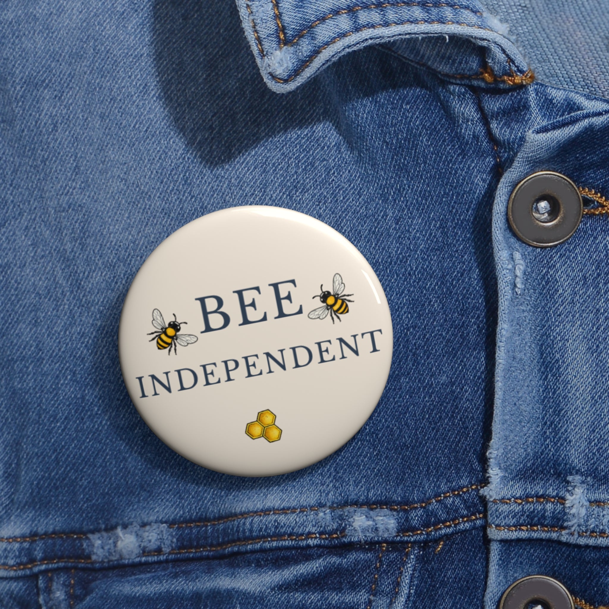 Bee pin badge on blue denim jacket, cream circle with BEE INDEPENDENT text and honeycomb