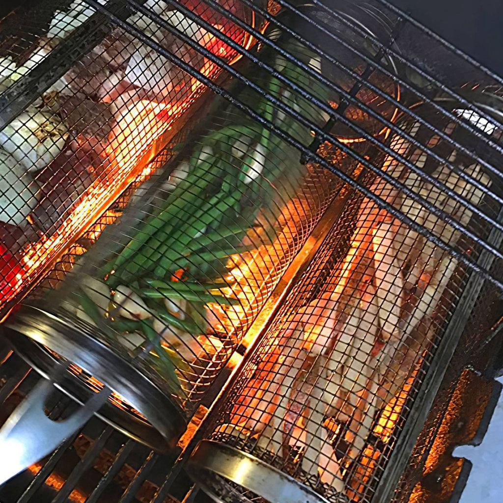 Stainless steel round grill baskets on a barbecue grill, holding food in wire mesh cylinders