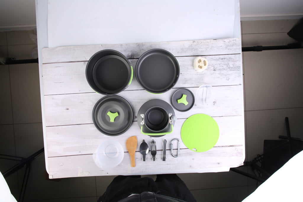 Assorted cookware pieces arranged together, including pots, pan, bowls, and lids with green accents