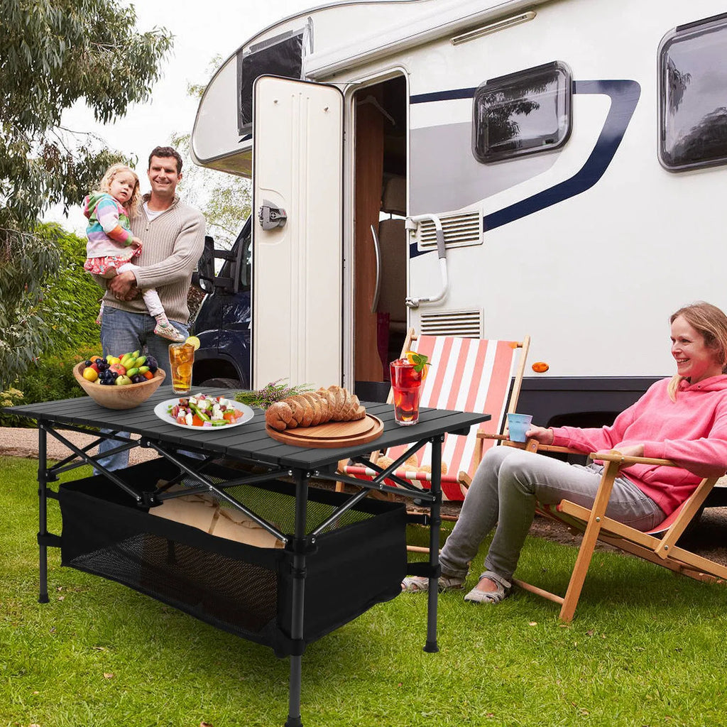 Black folding camping table with roll-up top, mesh basket, and drinks on the surface