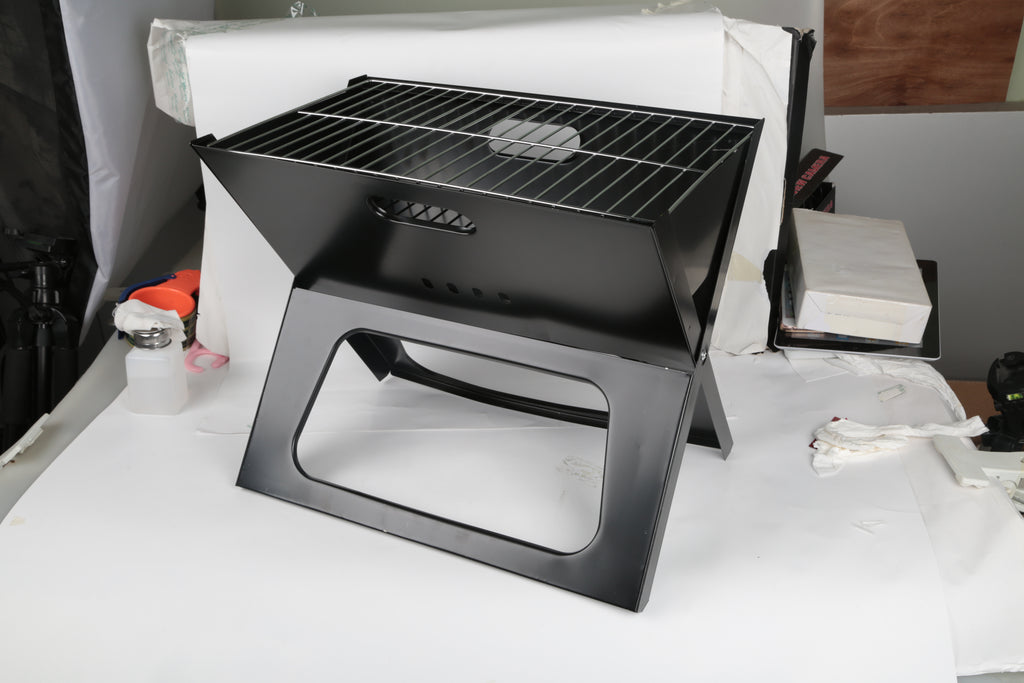 Black charcoal grill with cooking grate and front cutout window on the foldable base