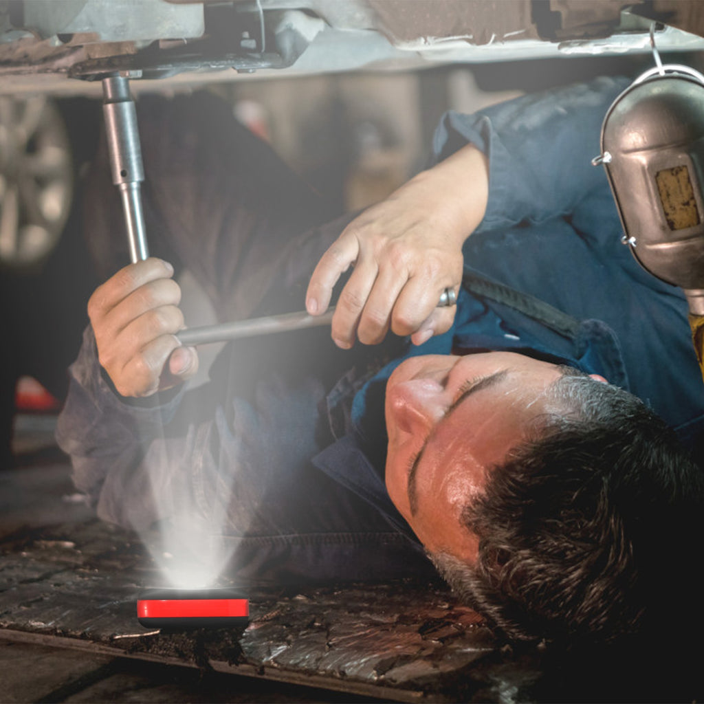 Portable LED work light projecting a beam in a workshop setting, red indicator light