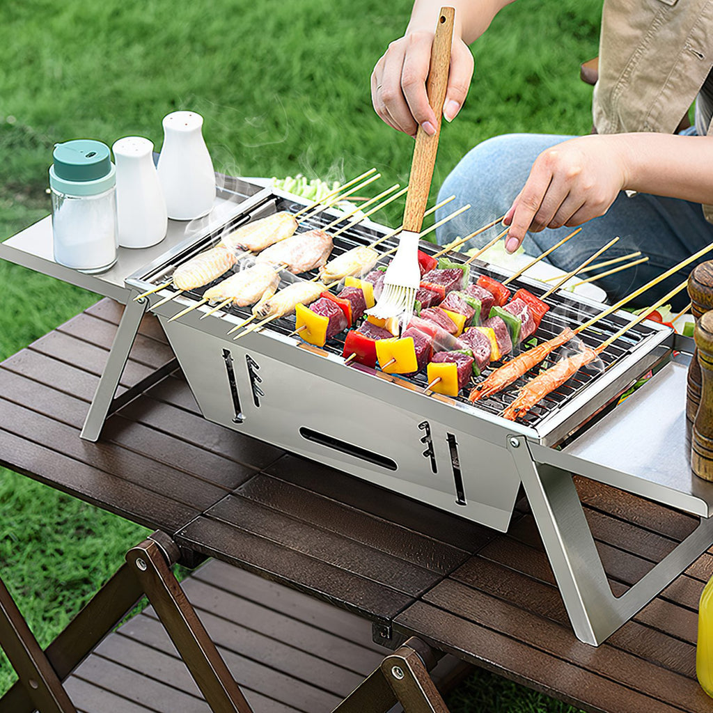 Foldable stainless steel grill with cooking grate, food on skewers and vegetables grilling