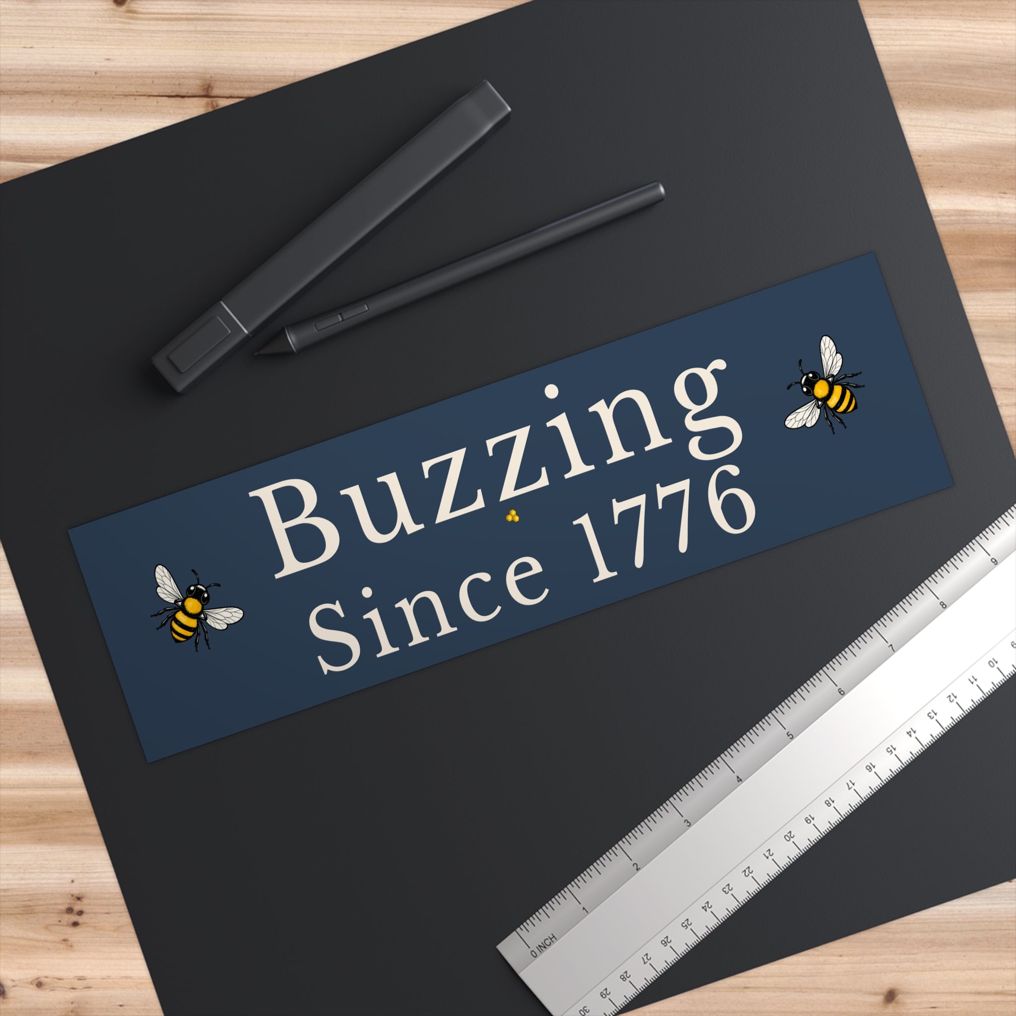Rectangle bumper sticker on a dark surface with 'Buzzing Since 1776' and bee icons