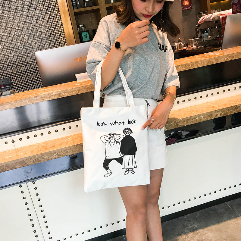 White canvas tote bag with graphic cartoon figures and short handles