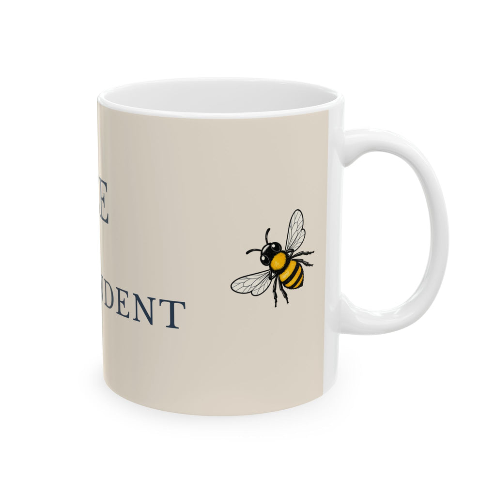 Beige ceramic mug with centered bee illustration and partial 'DENT' text, white handle