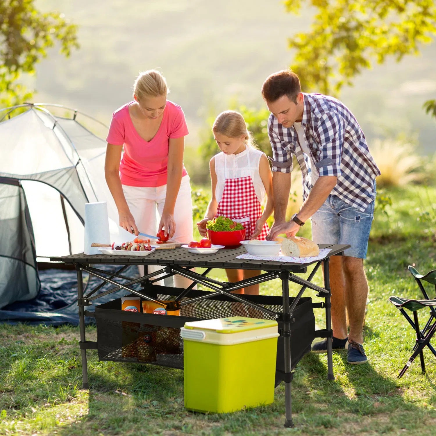 Black folding camping table with roll-up top and mesh basket, set for outdoor meals