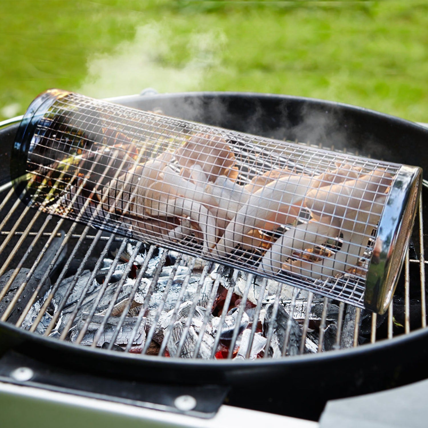 Round stainless-steel grill basket with wire mesh on BBQ grate, holding meat pieces