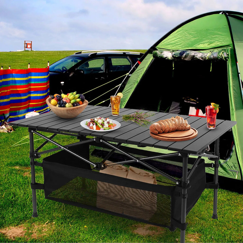 Black folding camping table with roll-up aluminum top and black mesh storage basket