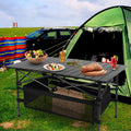 Black folding camping table with roll-up aluminum top and black mesh storage basket