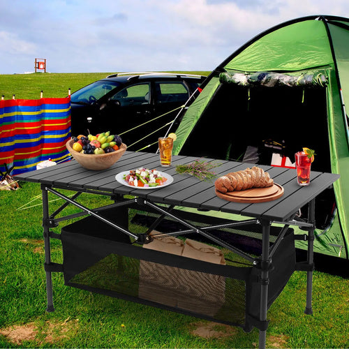 Black folding camping table with roll-up aluminum top and black mesh storage basket