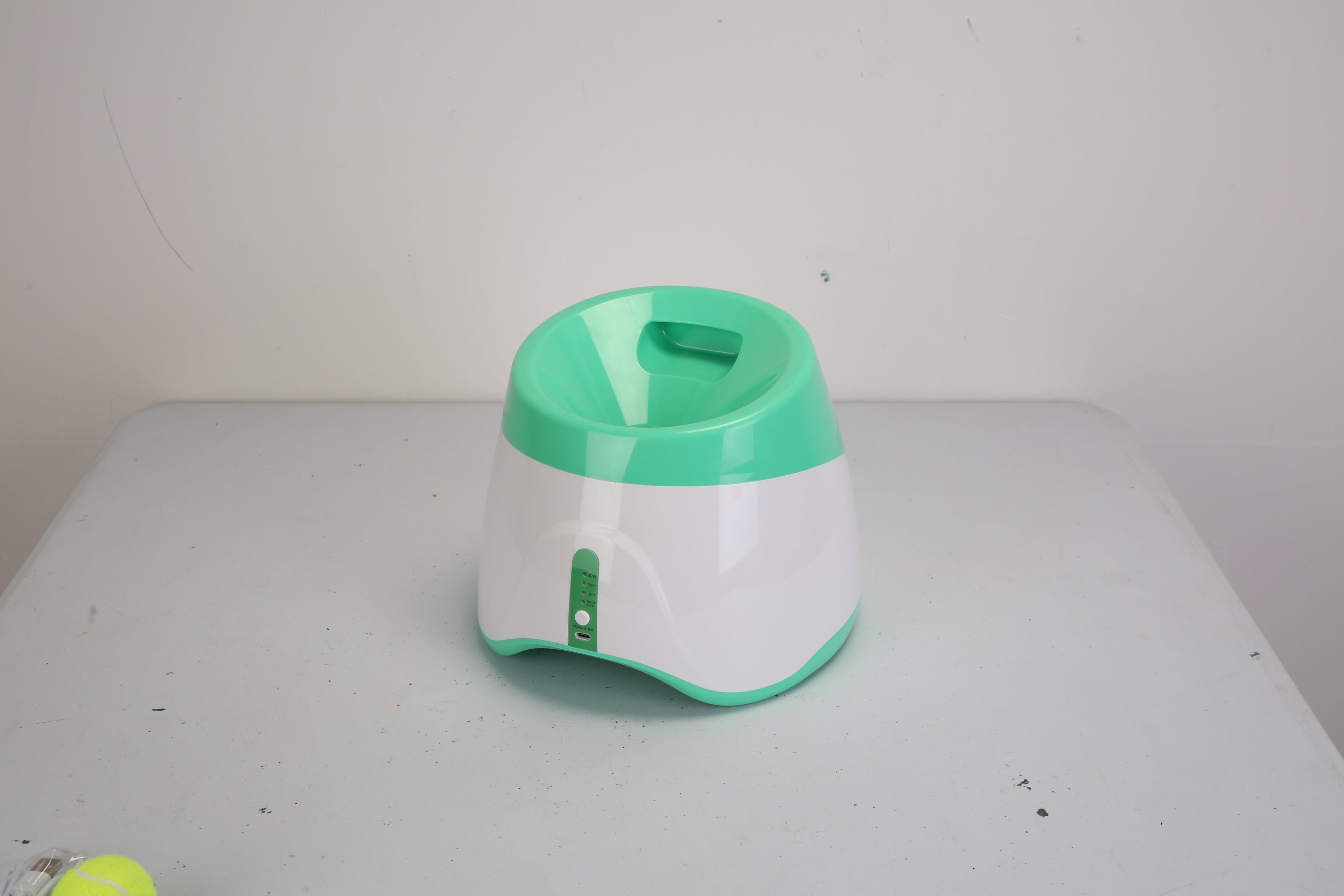 Green and white automatic dog ball launcher on a flat surface, front view