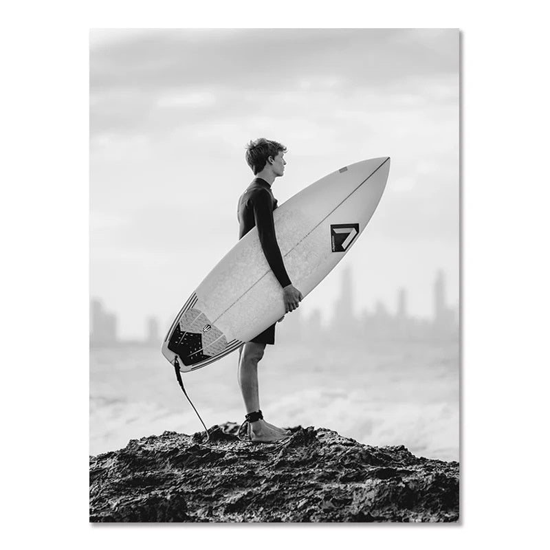 Black-and-white wall poster of surfer standing on board on rocky shoreline