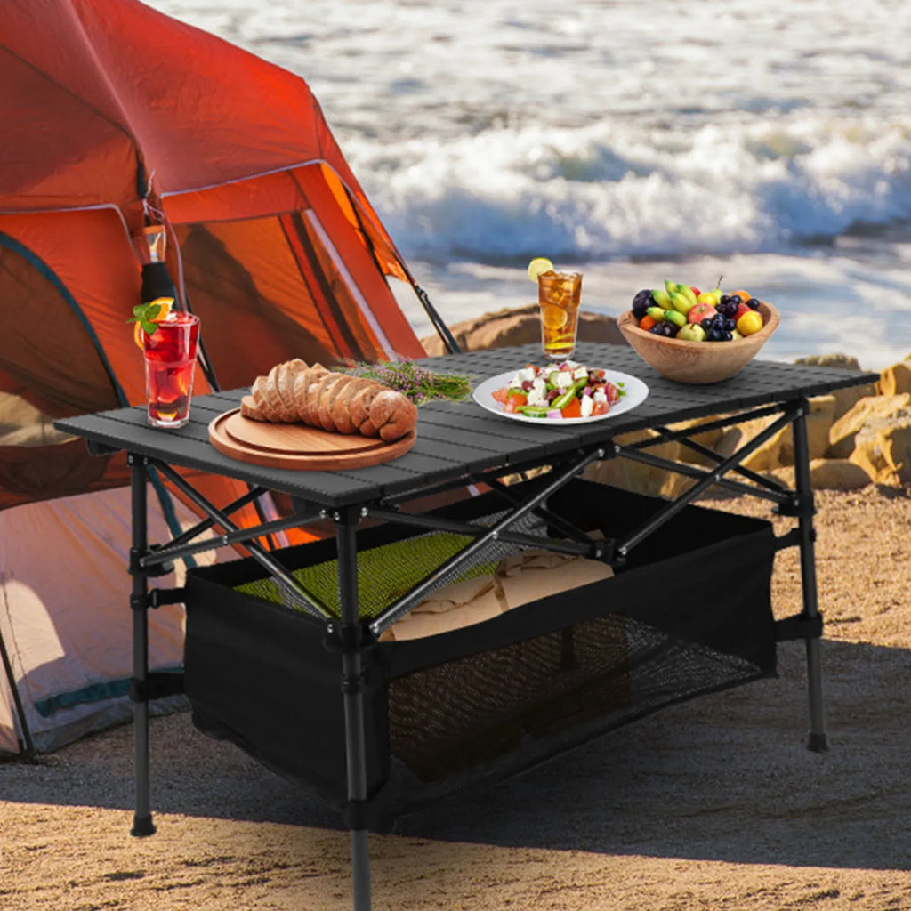 Black folding camping table with roll-up top and black mesh basket under the tabletop