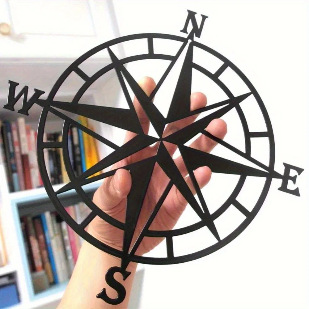 Compass rose metal wall art close-up, black star spokes within a circular ring and N, E, S, W