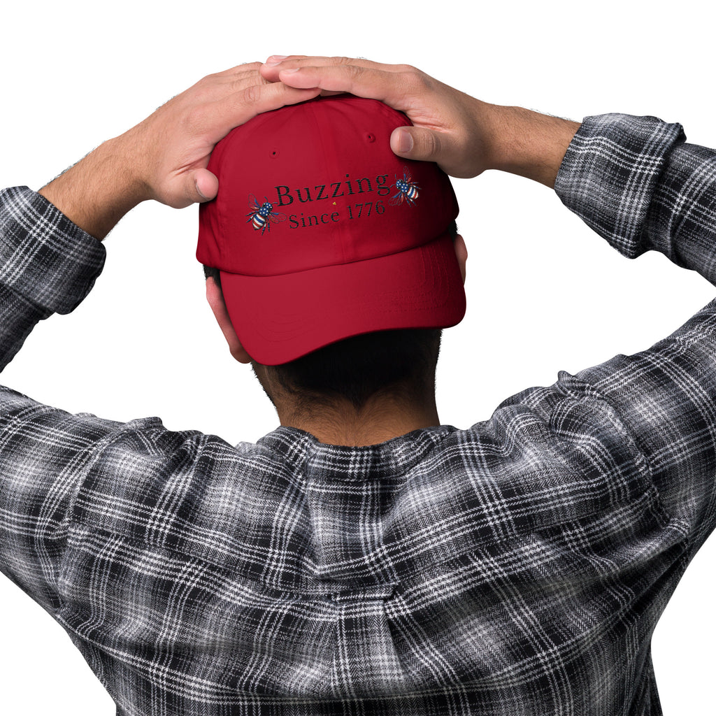 Cranberry red dad hat with embroidered “Buzzing Since 1776” on front