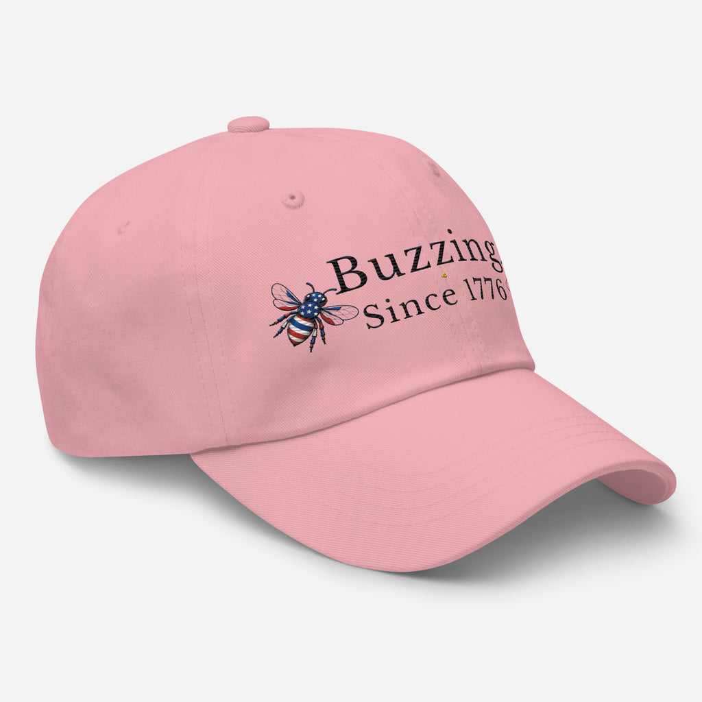 Light pink dad hat with embroidered bee and “Buzzing Since 1776” text on front