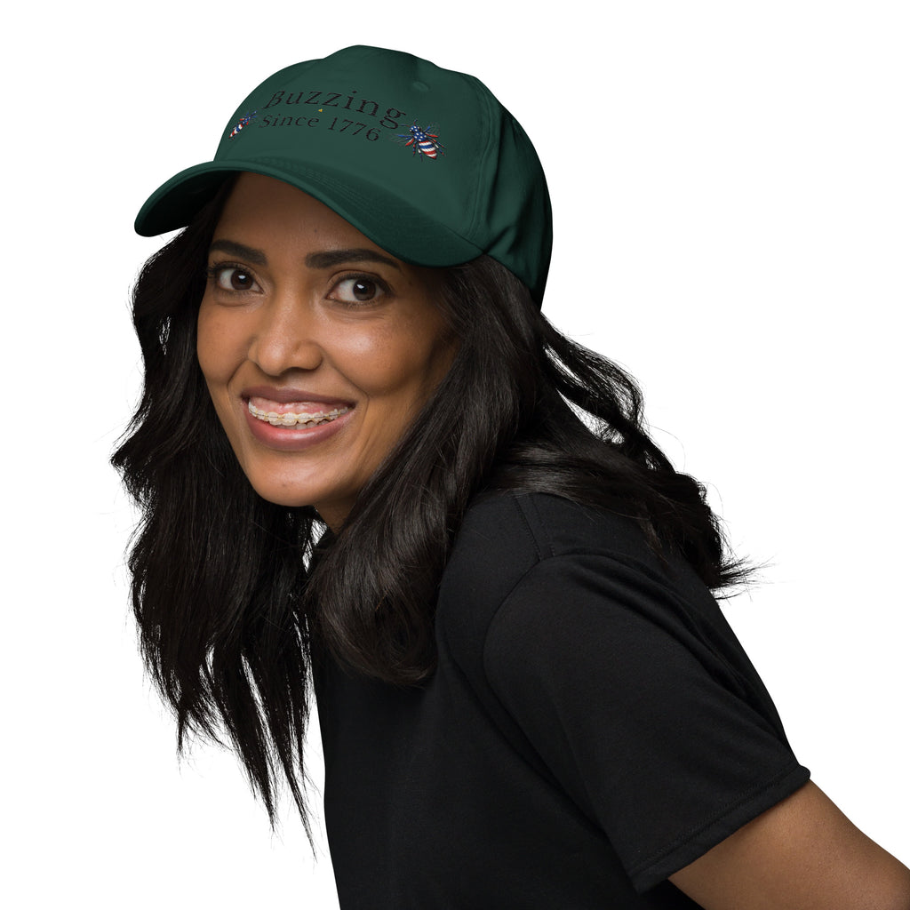 Spruce green dad hat with “Buzzing Since 1776” and bee graphic, worn
