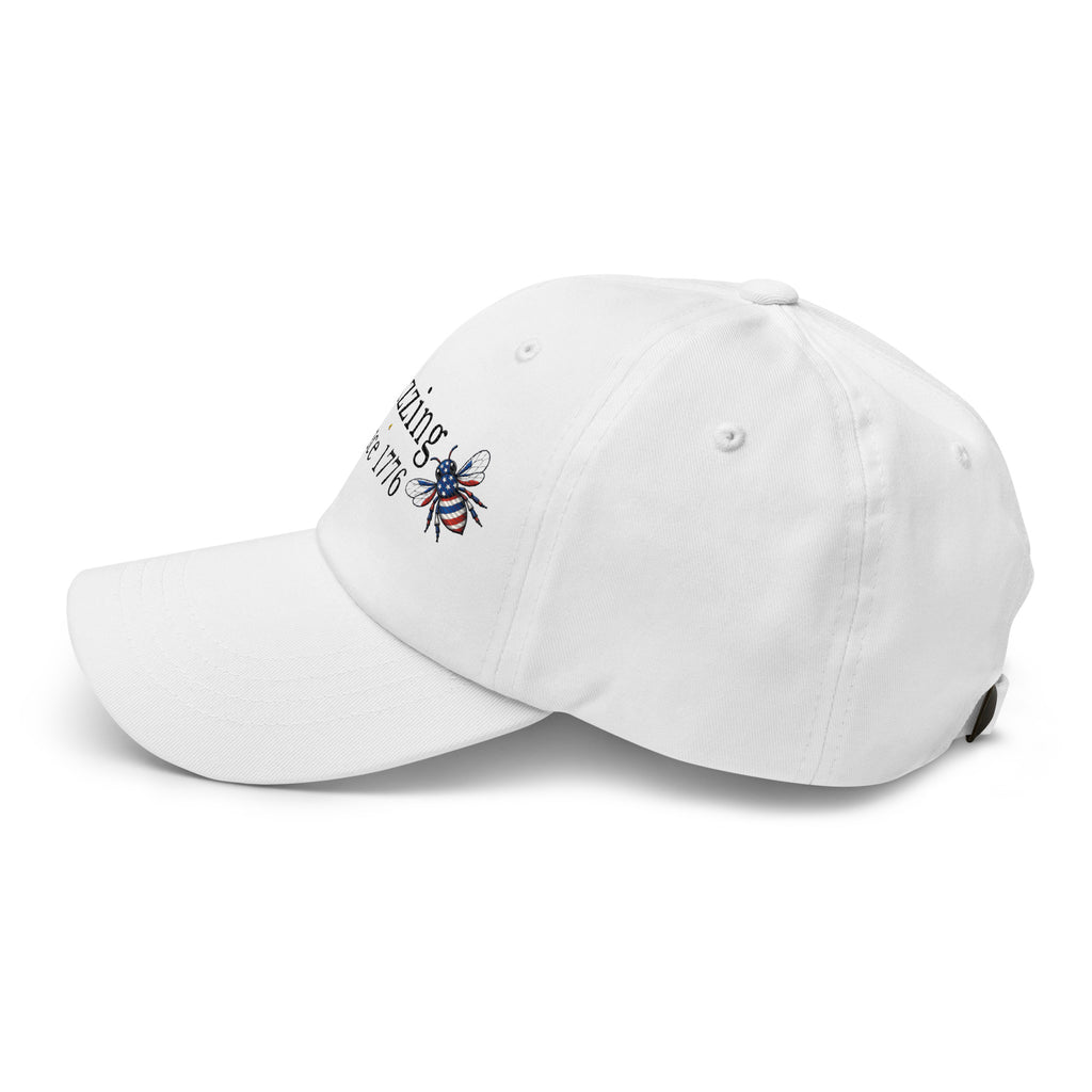 White dad hat with embroidered bee patch and “Buzzing Since 1776” text on front