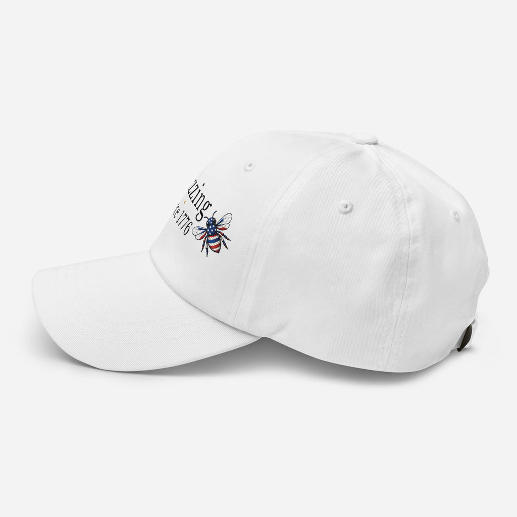White dad hat with embroidered bee and “Buzzing Since 1776” text on front