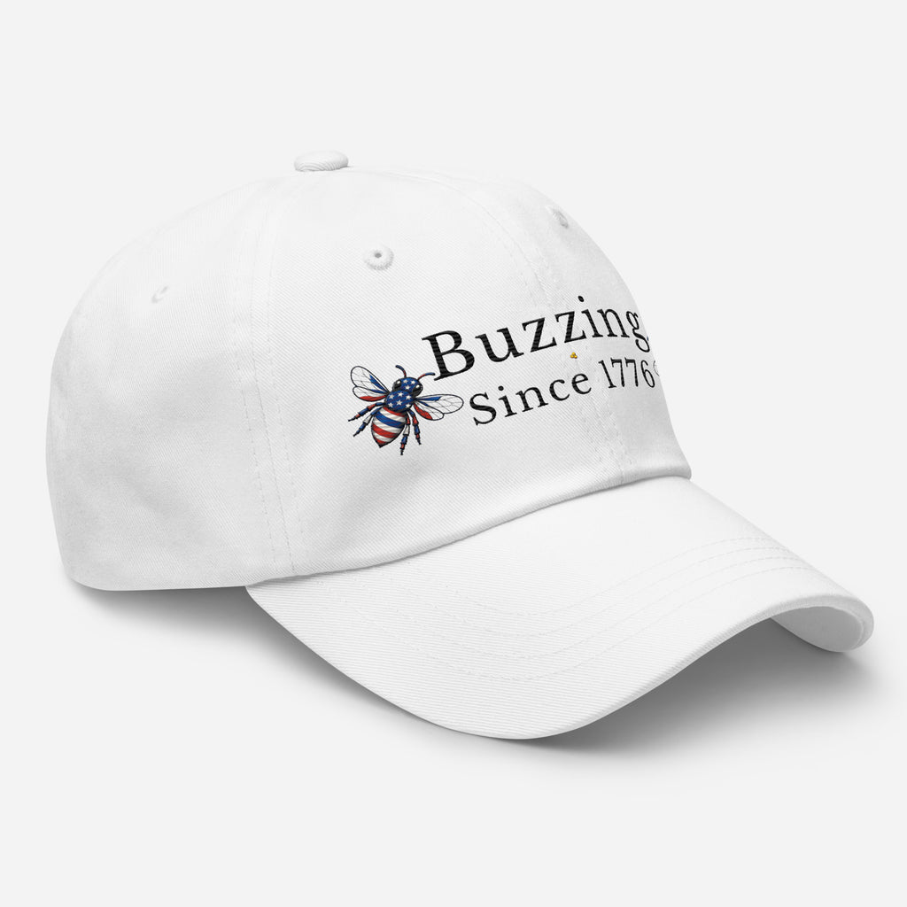 White dad hat with embroidered bee and “Buzzing Since 1776” text on front