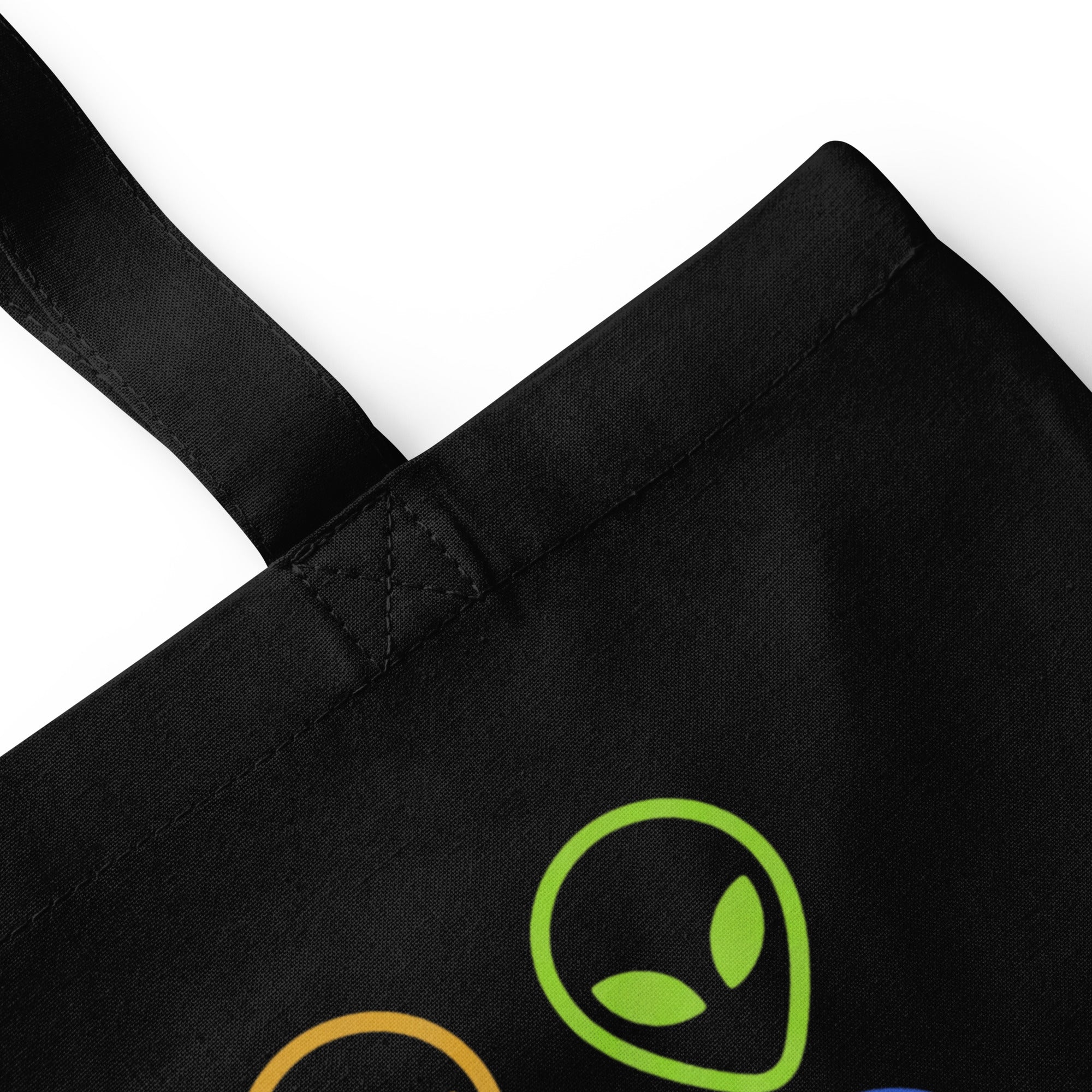 Black cotton tote bag close-up of strap seam and green alien face graphic.