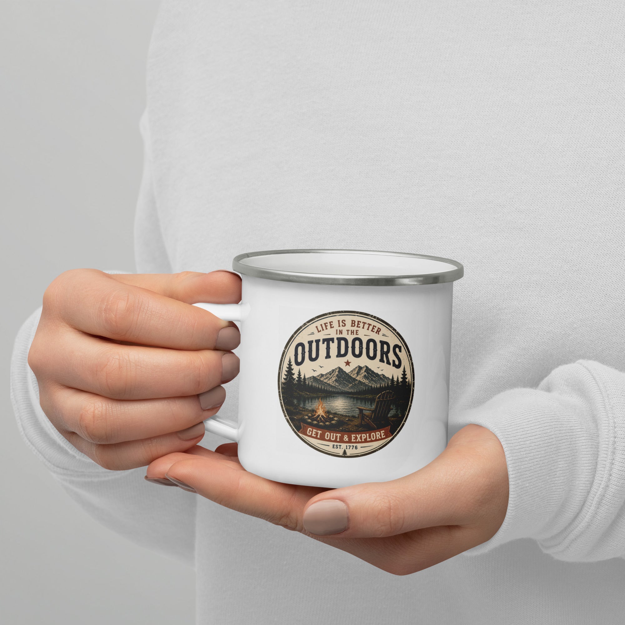 White enamel mug with silver rim held in hands, Outdoors logo visible