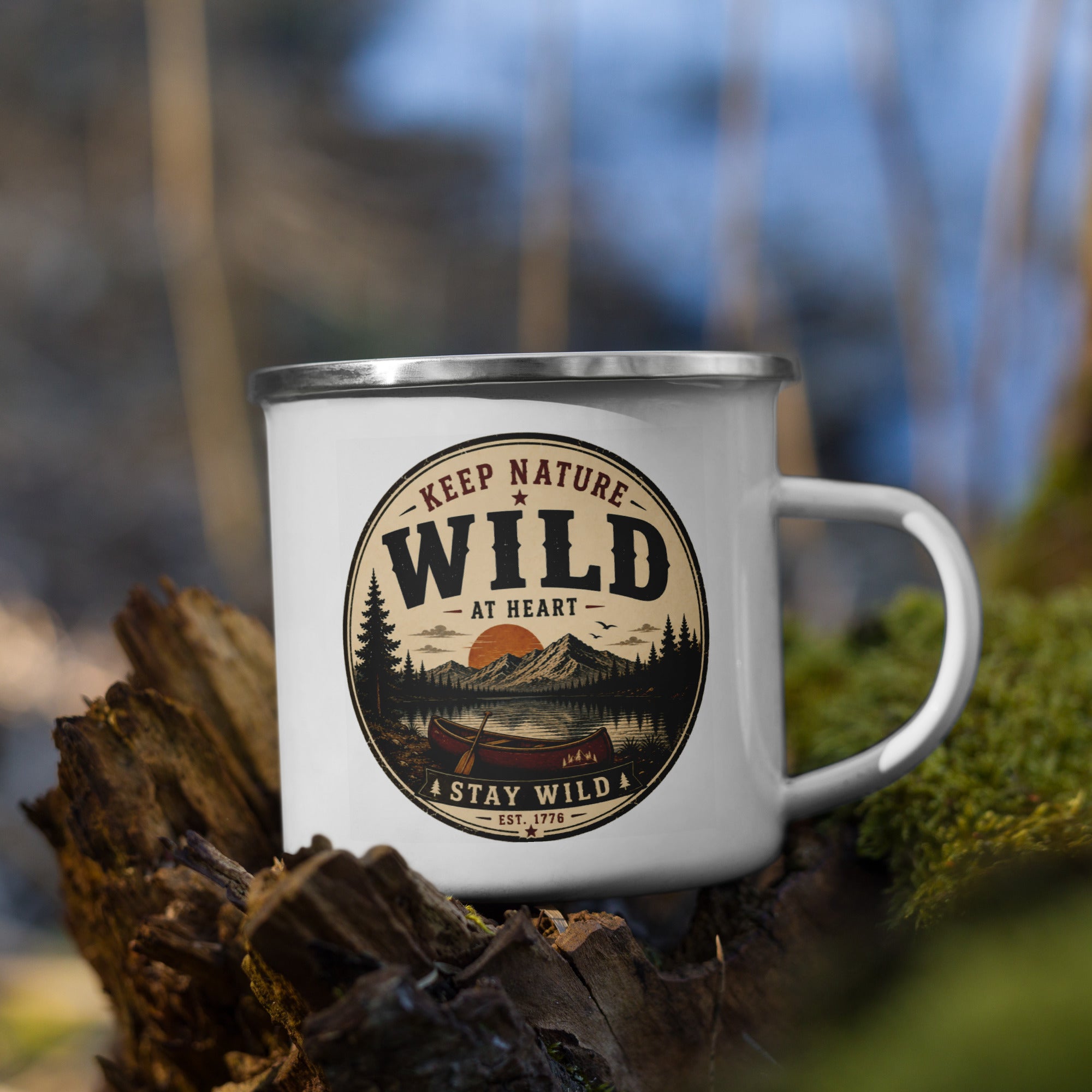 White enamel mug with silver rim and front logo, resting on rocks in outdoor setting.
