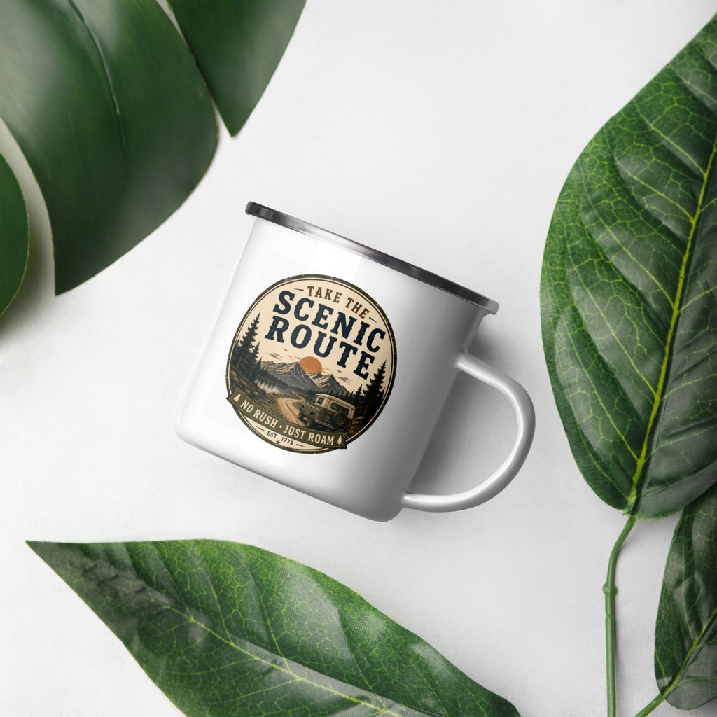 White enamel mug with Scenic Route logo, silver rim and handle, on a leaf background.