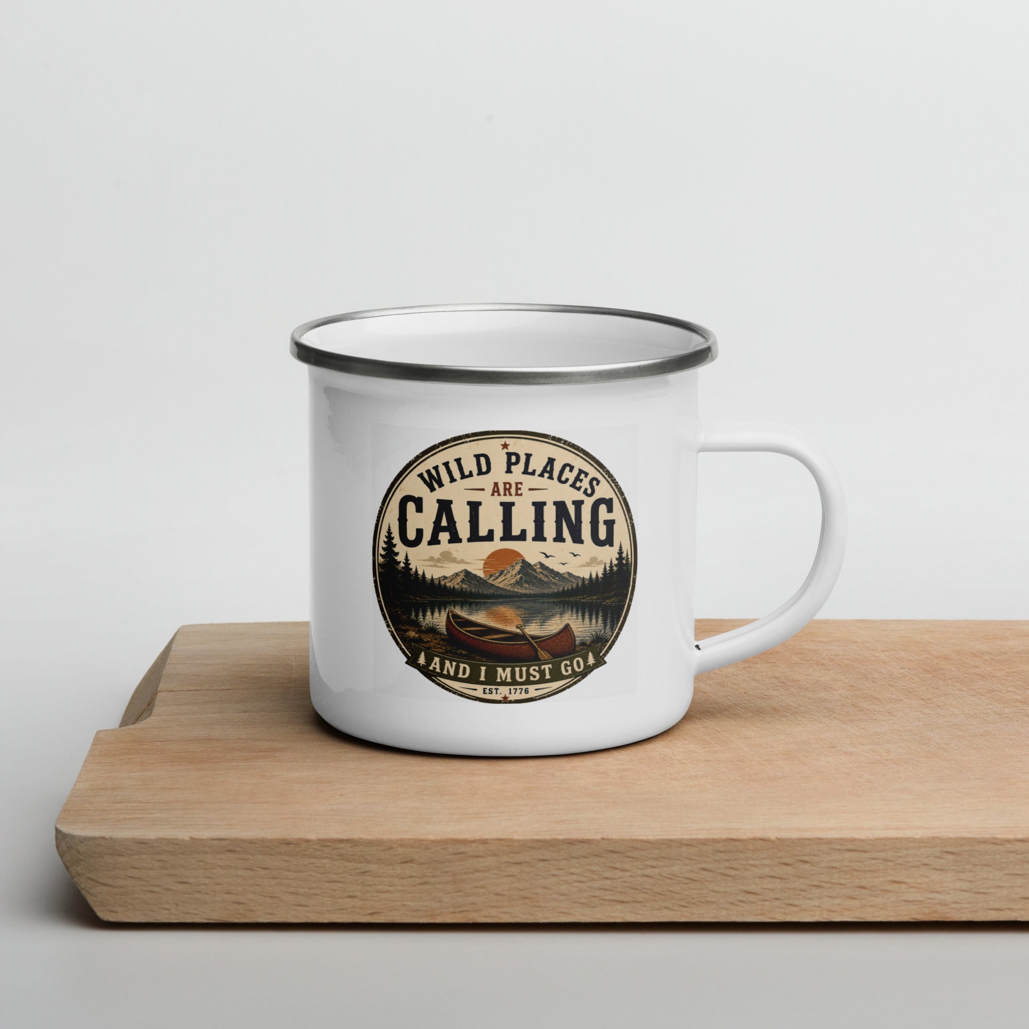 White enamel mug with silver rim and front graphic "WILD PLACES ARE CALLING" on wooden base