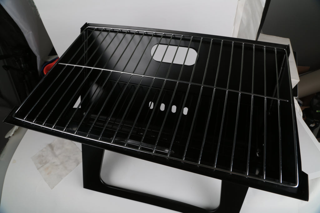 Black charcoal grill cooking grate with parallel bars and heat vents on the front panel