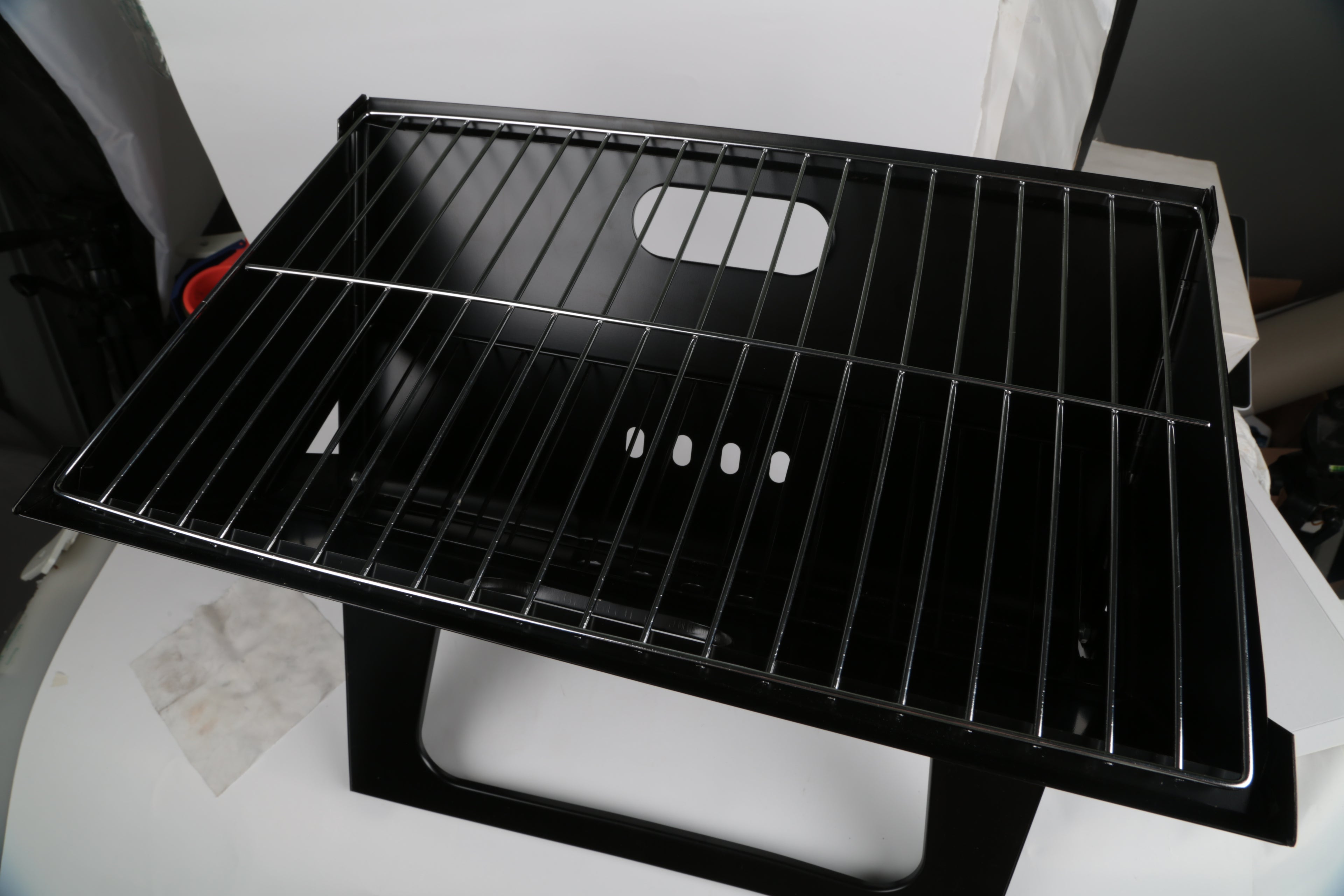 Black charcoal grill cooking grate with parallel bars and heat vents on the front panel