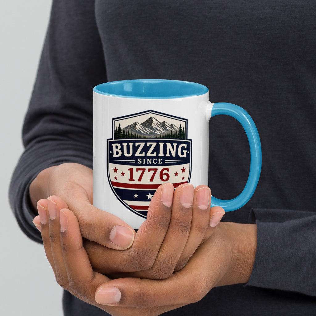 White mug with “Buzzing since 1776” graphic, blue interior and handle.