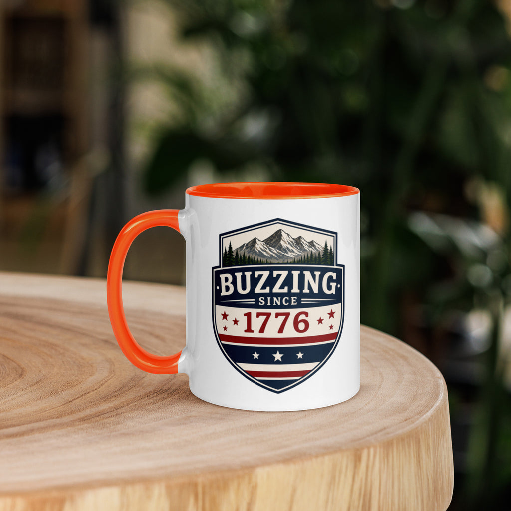 Mug with 'Buzzing Since 1776' crest, white body with orange handle and rim