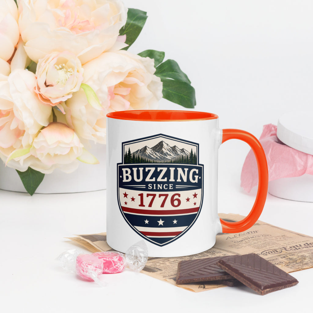 Ceramic mug with “1776” shield graphic, orange rim and handle, white body.