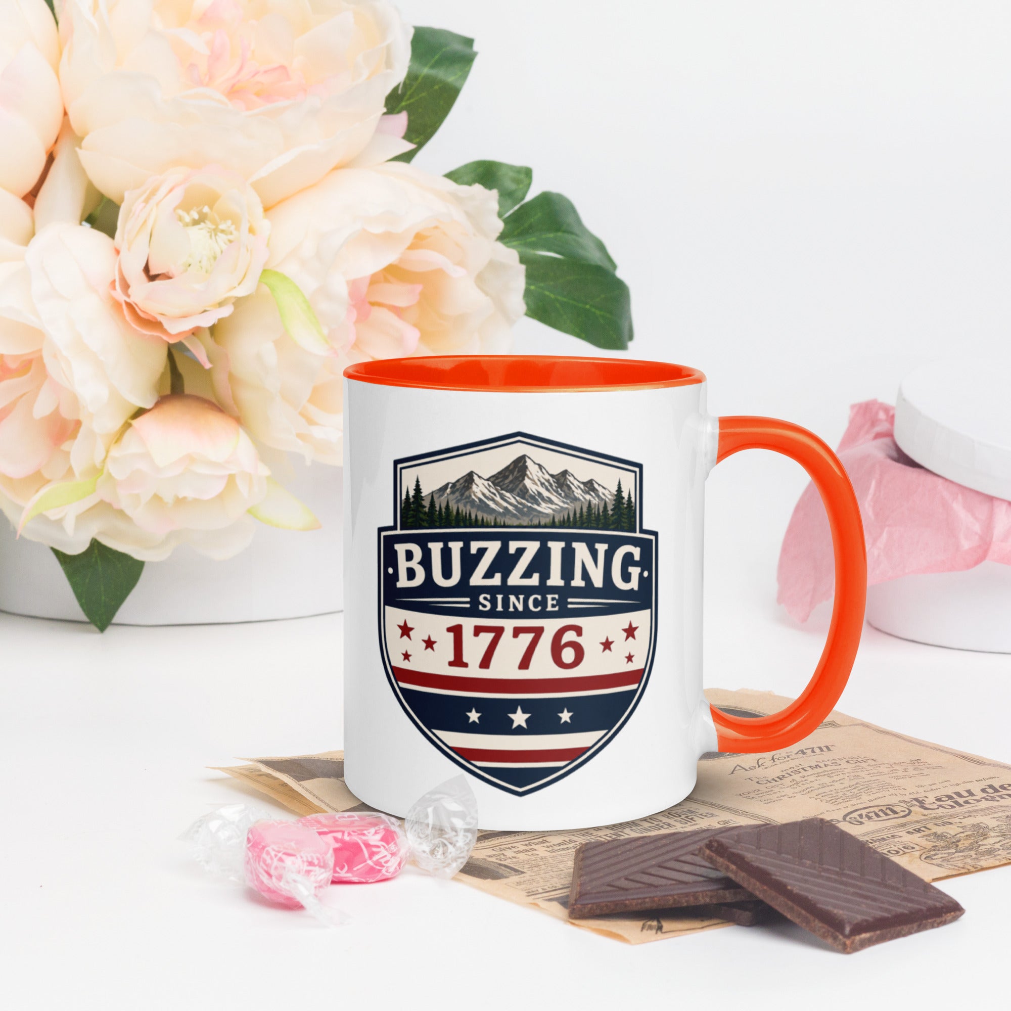 Ceramic mug with “1776” shield graphic, orange rim and handle, white body.