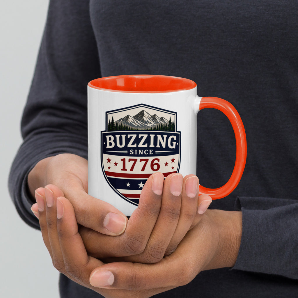 White mug with “Buzzing since 1776” graphic, orange interior and handle.