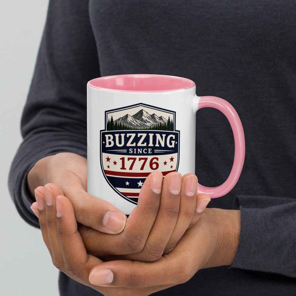 White mug with “Buzzing since 1776” graphic, pink interior and handle.