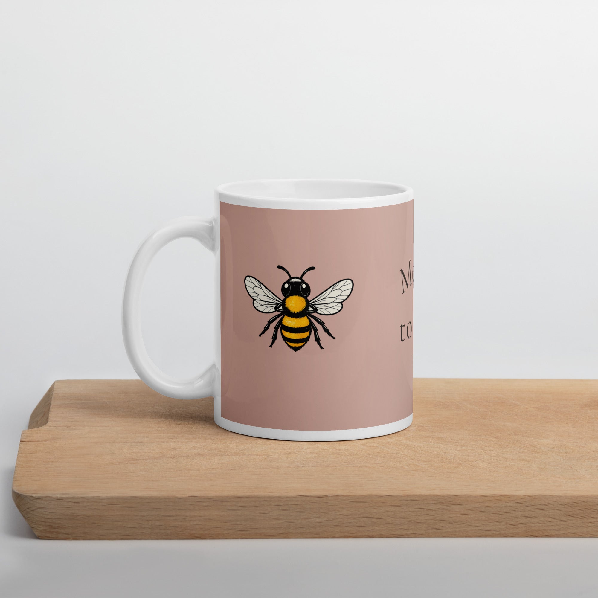 Dusty rose ceramic coffee mug with white rim, handle, and black-yellow bee illustration