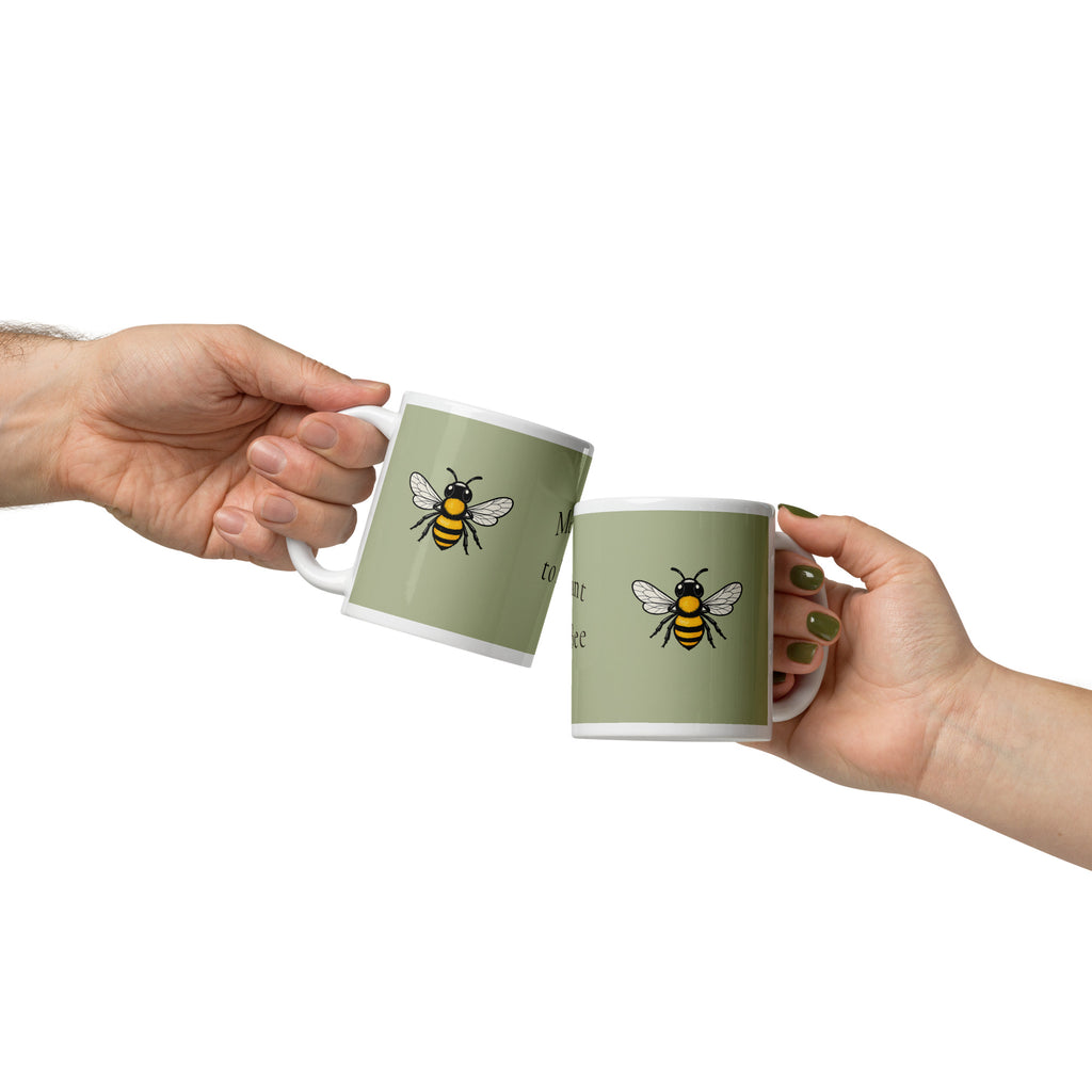 Sage green ceramic coffee mug with bee illustration, held in two hands