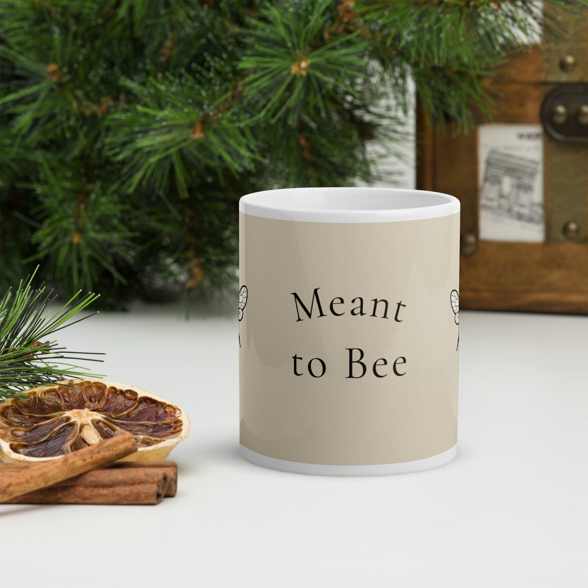 Light beige ceramic coffee mug with white rim, showing “Meant to Bee” text and bee