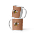 Two stacked brown ceramic coffee mugs with bee illustrations and white handles