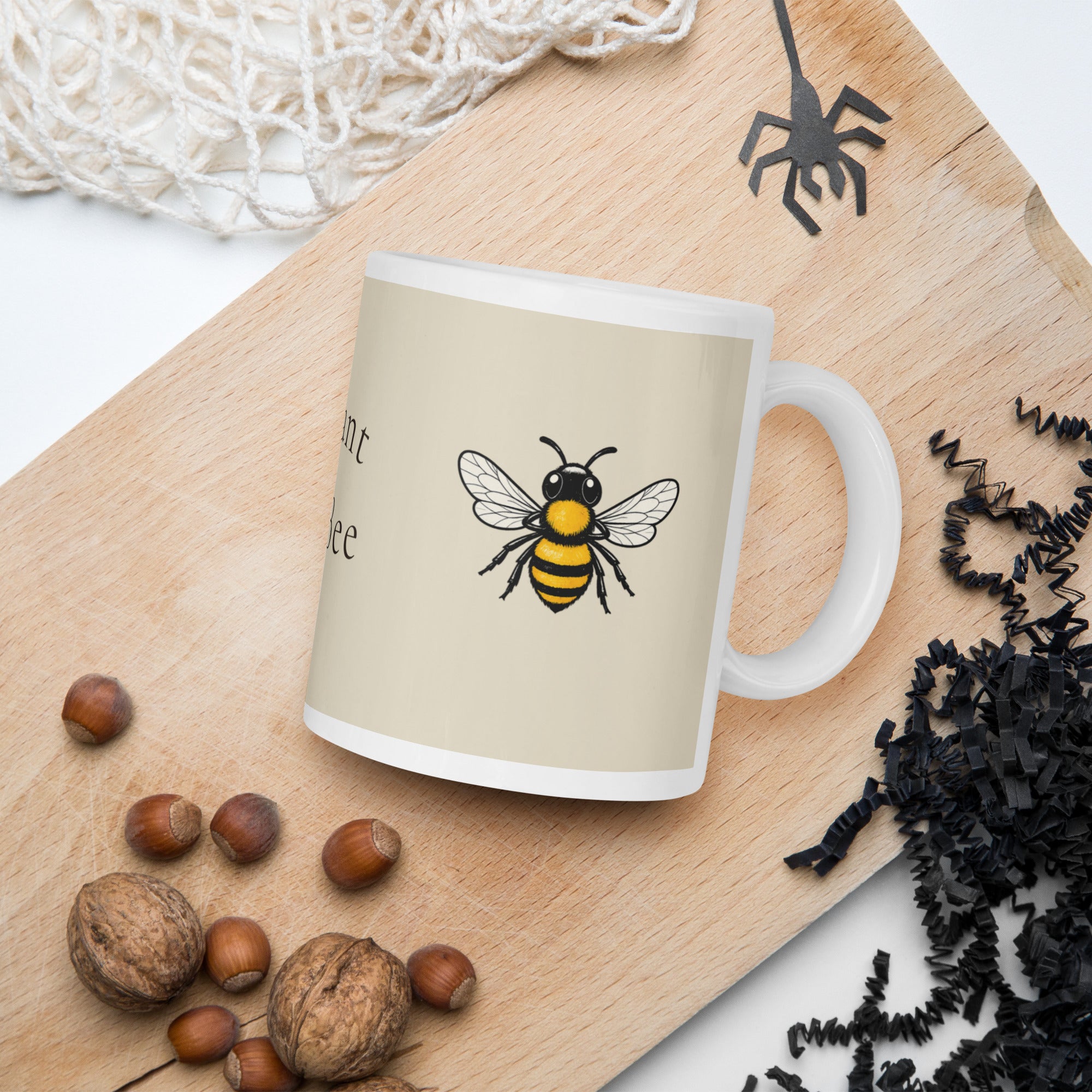 Light beige ceramic coffee mug with bee illustration on side, on wooden surface