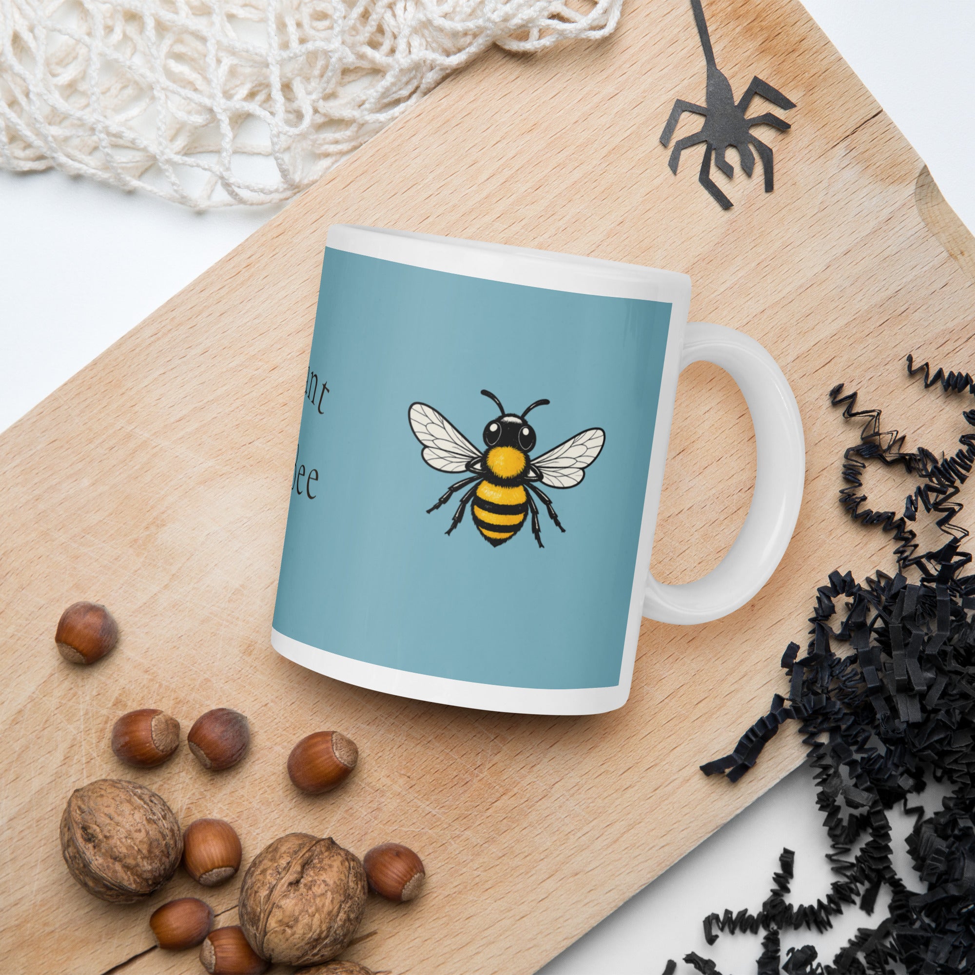 Blue ceramic coffee mug with bee illustration, handle visible, on wooden surface.