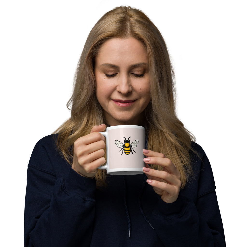Ceramic coffee mug with bee illustration, held by a woman in a navy hoodie