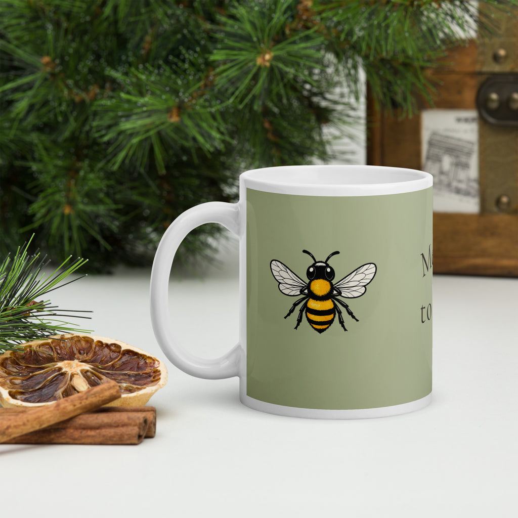 Sage green ceramic mug with bee illustration and white handle on a surface